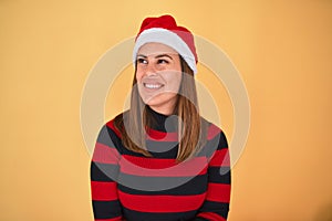 Young beautiful woman smilling happy wearing striped sweater and a santa claus hat at christmas over yellow background