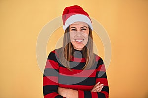 Young beautiful woman smilling happy wearing striped sweater and a santa claus hat at christmas over yellow background