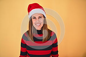Young beautiful woman smilling happy wearing striped sweater and a santa claus hat at christmas over yellow background