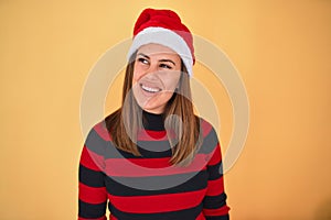Young beautiful woman smilling happy wearing striped sweater and a santa claus hat at christmas over yellow background