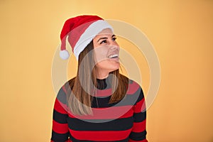 Young beautiful woman smilling happy wearing striped sweater and a santa claus hat at christmas over yellow background