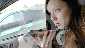 Young beautiful woman speak a voice message on a mobile phone sitting in the car.