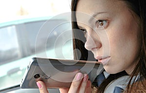 Young beautiful woman speak a voice message on a mobile phone sitting in the car and smiles.