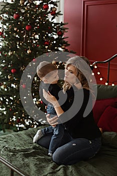 Young beautiful woman spends Christmas time with her cute little son in the interior decorated for New year& x27;s holidays