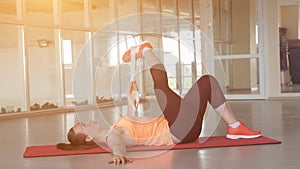 Young beautiful woman in sports clothes doing warm-up on the rug in the gym with tape.