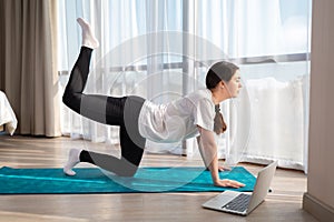 Young beautiful woman in sports clothes, doing yoga online lessons on a laptop. Indoor. Side view. The concept of online training