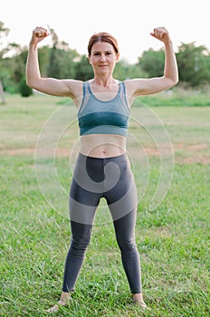 Young beautiful woman in sportswear demonstrates her biceps. Sporty physique woman posing in nature