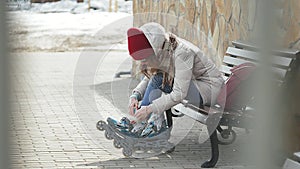 Young beautiful woman in sporty warm clothes and rollers, sitting on a wooden bench and dresses roller skates getting