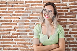 Young beautiful woman standing over bricks wall smiling looking to the side and staring away thinking