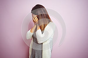 Young beautiful woman standing over pink isolated background with sad expression covering face with hands while crying