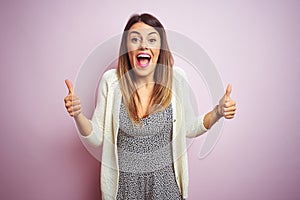 Young beautiful woman standing over pink isolated background success sign doing positive gesture with hand, thumbs up smiling and