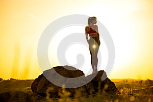 Young Woman Standing on the Rock at Hot Beautiful Summer Sunset. Adventure and Healthy Active Lifesyle Concept photo