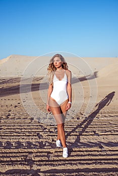 Young beautiful woman standing summer sandy beach, tanned skin, white sneakers body. The concept fashion, style, trend