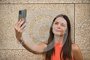 Young beautiful woman with straight brown hair and orange top, making a video call with her cell phone. Concept fashion, beauty,