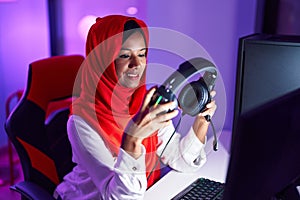 Young beautiful woman streamer smiling confident holding headphones at gaming room