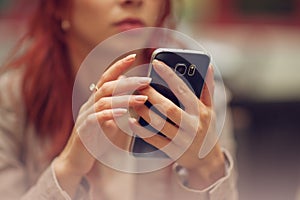 Young beautiful woman in a street cafe, is busy with her cell phone, close up at hands holding mobile phone