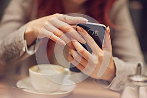 Young beautiful woman in a street cafe, is busy with her cell phone, close up at hands holding mobile phone