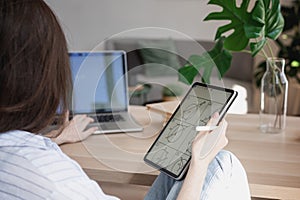 Young beautiful woman student with digital tablet and laptop studying working at home at the table