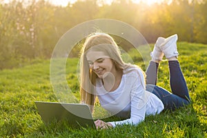 Young beautiful woman student with a laptop lies on the grass, in sunset