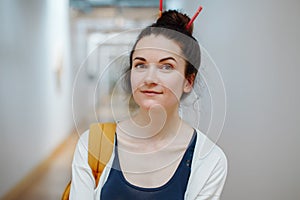 young beautiful woman student with pencils in hair bun, standing in hall of college university