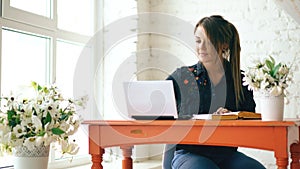 Young beautiful woman student sitting with laptop and writing book at cafe indoors