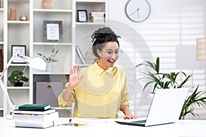 Young beautiful woman studying online sitting at desk in home office, female student in yellow shirt using laptop to