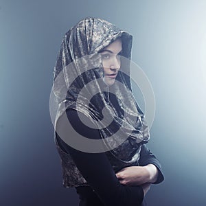 Young beautiful woman in stylish Cape with hood. Portrait on dark background, smoke and fog