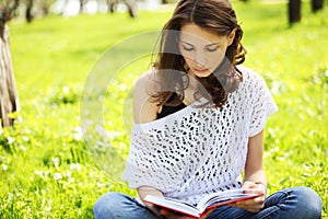 Young beautiful woman in summer park reading a book