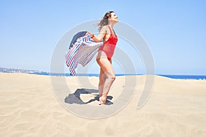 Young beautiful woman sunbathing with open arms holding towel at maspalomas dunes bech