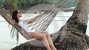 Young beautiful woman in sunglasses relaxing on the hammock on tropical beach