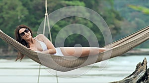 Young beautiful woman in sunglasses relaxing on the hammock on tropical beach