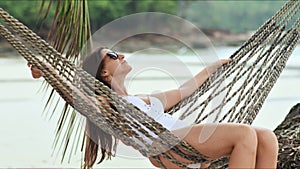Young beautiful woman in sunglasses relaxing on the hammock on tropical beach