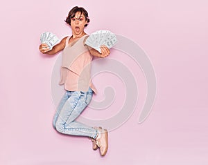 Young beautiful woman surprised holding dollars banknotes 