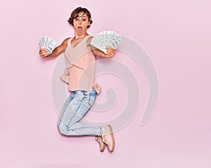 Young beautiful woman surprised holding dollars banknotes 