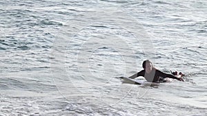 A young beautiful woman is swimming at the ocean on her surfboard.
