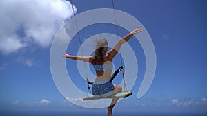 Young beautiful woman on the swing with sea and sky background in slow motion. Concept of freedom and happiness