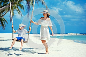 Young beautiful woman swinging her son on a tropical beach, Koh Phangan island. Thailand