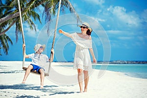 Young beautiful woman swinging son on a tropical beach, Koh Phangan island. Thailand.