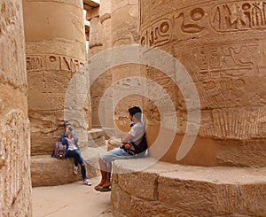 Young beautiful woman taking pictures between the columns of the hypostyle hall of Karnaks temple in Luxor, Egypt