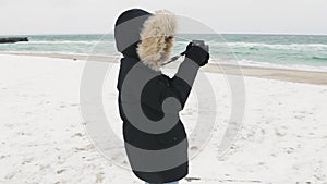 Young beautiful woman taking pictures of the sea on a cold winter day. Slow motion