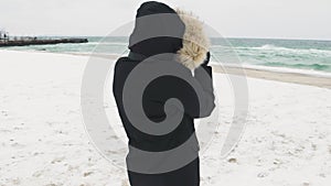 Young beautiful woman taking pictures of the sea on a cold winter day. Slow motion