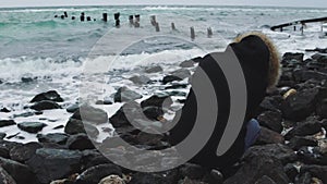 Young beautiful woman taking pictures of the sea on a cold winter day. Slow motion