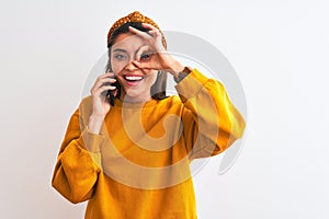 Young beautiful woman talking on the smartphone standing over isolated white background with happy face smiling doing ok sign with