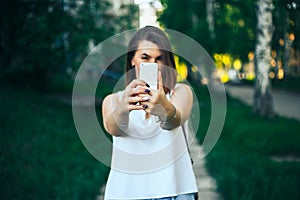 young beautiful woman, teenager, making selfie in park, girl is unfocused, focus on smartphone