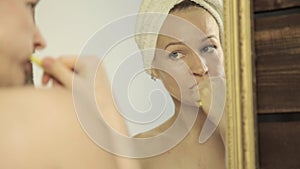 Young beautiful woman with towel on a head brushing her teeth in bathroom