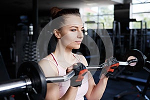 Young beautiful woman training biceps with barbell