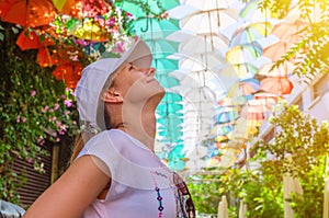 Young beautiful woman traveler looking up at colorful multicolored umbrellas above head