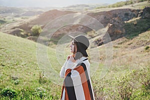 Young beautiful woman traveler wearing hat and poncho relaxing on the top of the hill