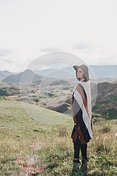 Young beautiful woman traveler wearing hat and poncho relaxing on the top of the hill