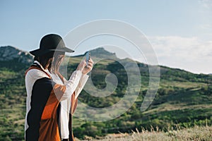 Young beautiful woman traveler wearing hat and poncho taking pictures on her smart phone